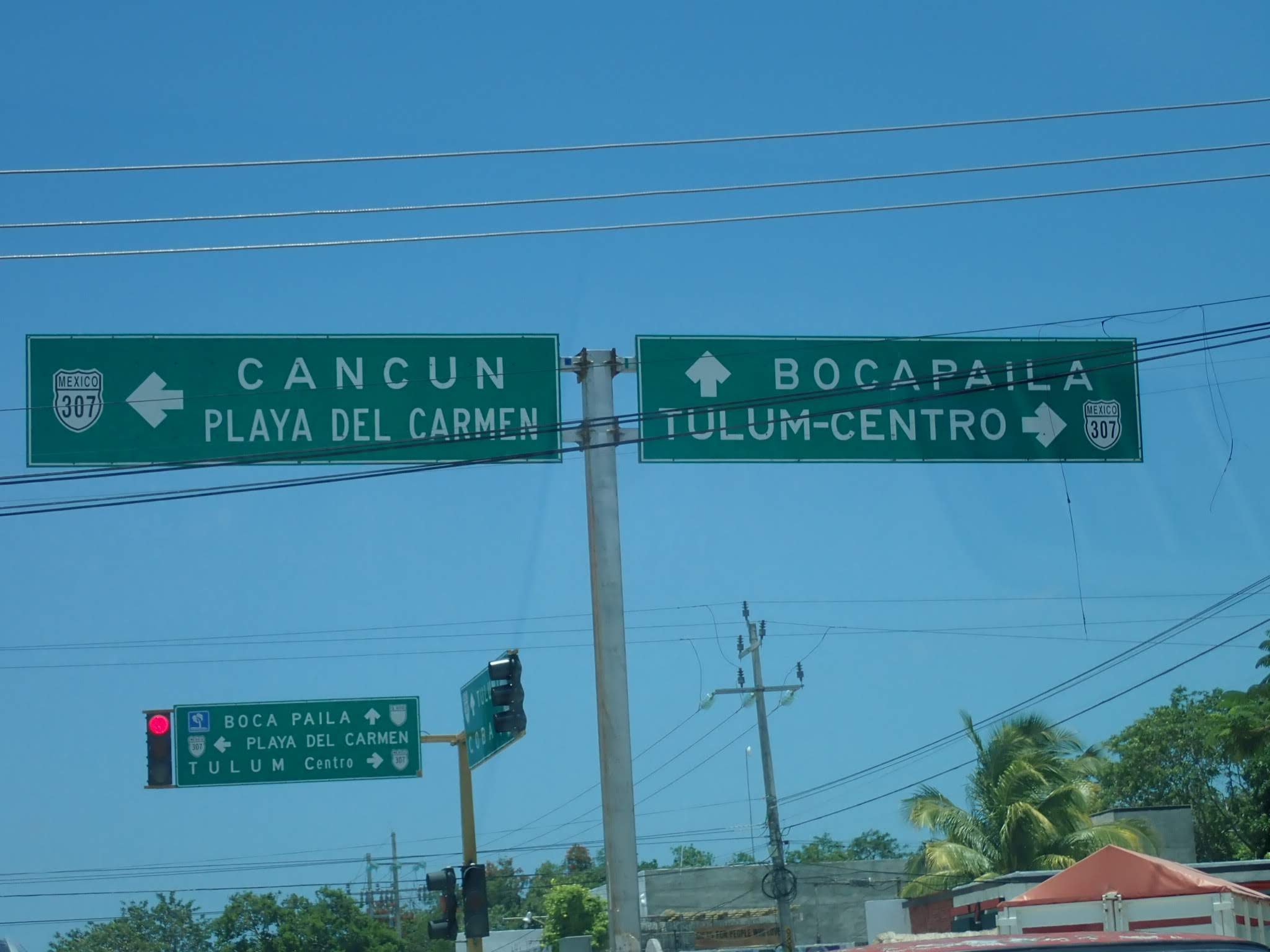 Two over head Street signs.The sign to the left reads Cancun and Playa del Carmen. The right sign reads Bocapaila and Tulum-Centro. There are other signs, and electrical wires.